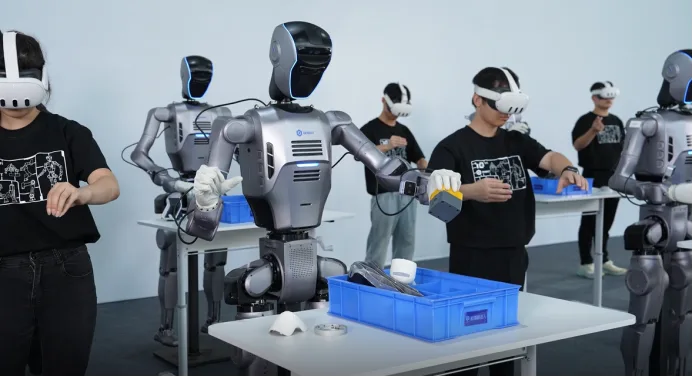 Humanoid robotok VR-ral betanított operátorok mellett.